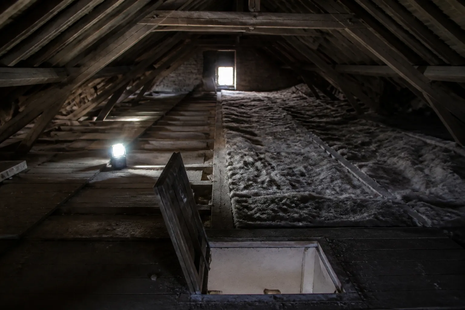 Combles en cours d’isolation, isolant déroulé entre solives sur une moitié, plancher de comble nu sur l’autre et trappe d’accès ouverte